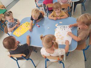 Dzieci przyklejają na słoiczki warzywa i owoce tworząc jesienne przetwory