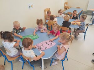 Dzieci przyklejają na słoiczki warzywa i owoce tworząc jesienne przetwory