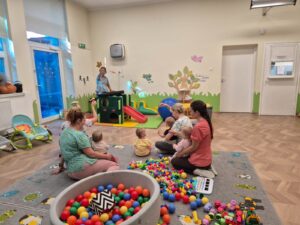 Dzieci z opiekunkami słuchają piosenek na zajęciach rytmiki.