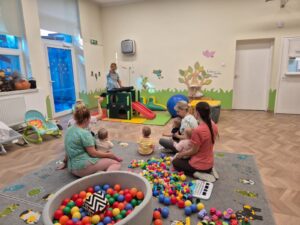 Dzieci z opiekunkami słuchają piosenek na zajęciach rytmiki.