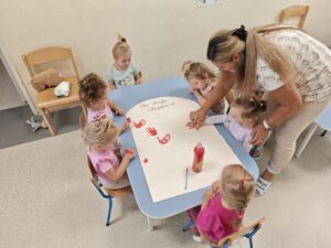 Dzieci odbijają rączki pomalowane czerwoną farbą tworząc serce na brystolu